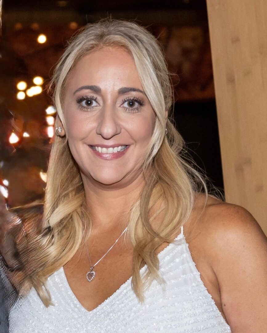 Smiling woman with blonde hair in a white top at an indoor event.